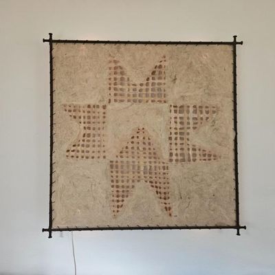 Contemporary lighted wall art featuring a starburst pattern on textured handmade paper, stretched over a dark metal frame.