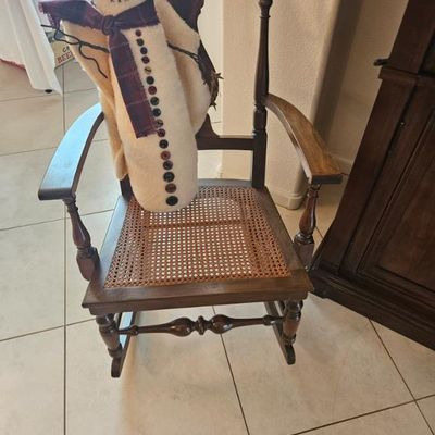 Vintage wooden rocking chair with a woven cane seat, turned spindles, and a decorative plush snowman figure resting on the arm.