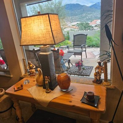 Rustic pine console table featuring a tall ceramic table lamp with a burlap shade, flanked by decorative pottery and small figurines.