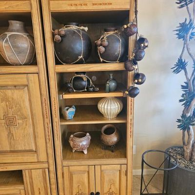 Southwestern-style light oak bookcase displaying an assortment of rustic pottery, ceramic vases, and decorative hanging gourds.