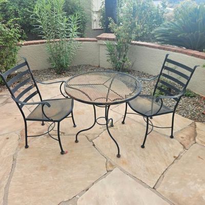 Three-piece black wrought iron bistro set featuring a round mesh-top table and two matching armchairs with slatted backs.