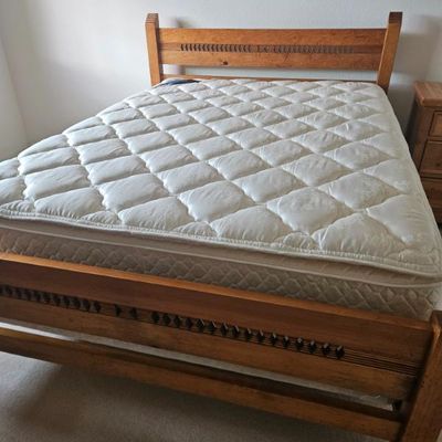 Rustic oak bed frame with carved geometric details on the headboard and footboard, complete with mattress and box spring.