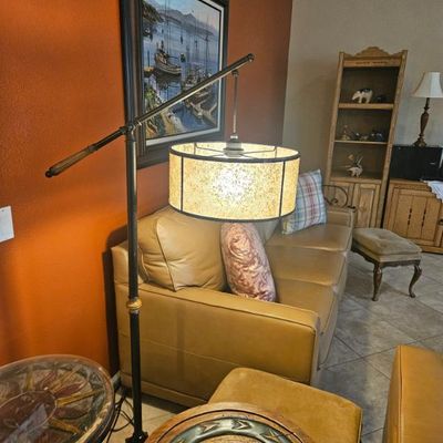 Vintage metal bridge arm floor lamp with a drum shade, shown alongside a tan leather sofa and rustic wooden accent tables.