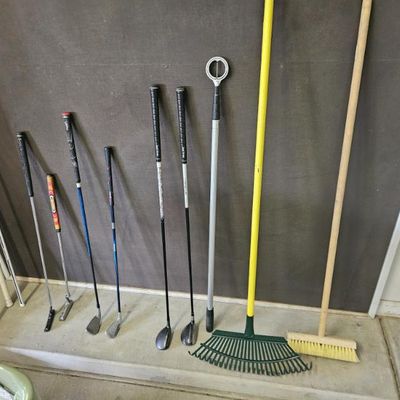 Assorted golf clubs, a golf ball retriever, a green plastic leaf rake, and a wooden push broom 