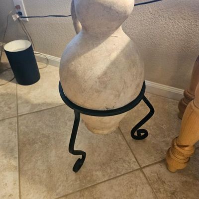 Rustic terracotta amphora vase with a single handle, displayed on a black wrought iron tripod stand.