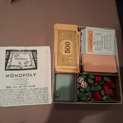 1935 MONOPOLY GAME AND ANTE-UP-RUMMY BOARD WITH MARBLES STORED IN THE FRAME PLUS PLAYING CARDS