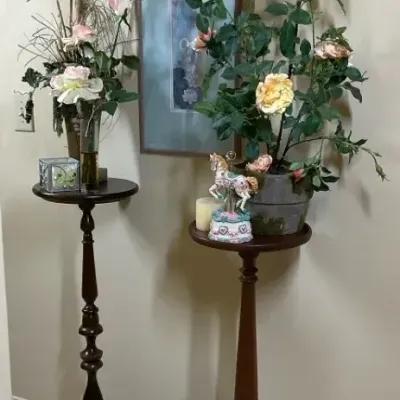 Two Wooden Pedestal Tables with Floral Arrangements and Framed Art