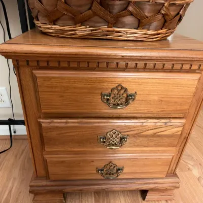 Oak three-drawer nightstand with brass pulls, woven basket
