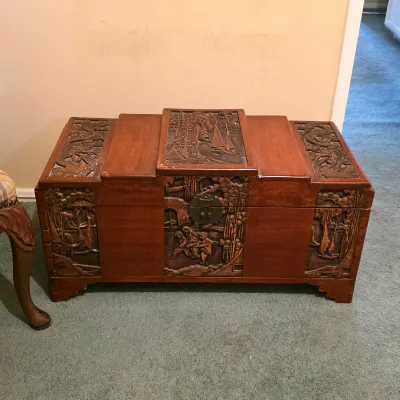 Carved Asian-style wooden trunk with decorative panels, figural scenes and raised feet.