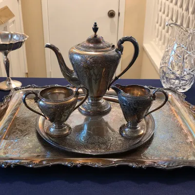 Ornate silverplate tea service with lidded pot, creamer, sugar bowl and handled serving tray.