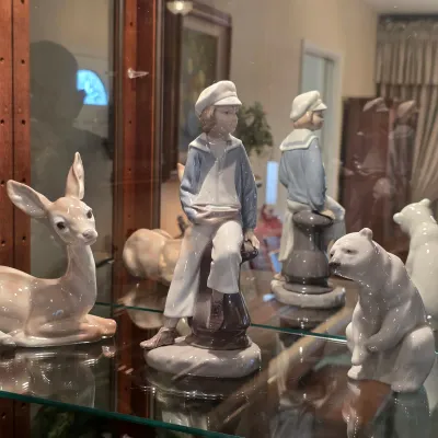 Lladro porcelain sailor boy holding a model sailboat, displayed with deer and polar bear figurines.