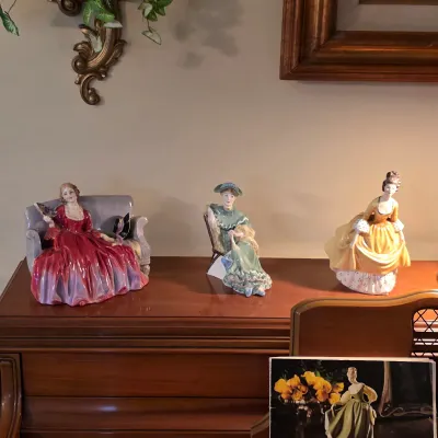 Royal Doulton porcelain figurines displayed atop the piano, featuring seated and standing ladies in colorful gowns.