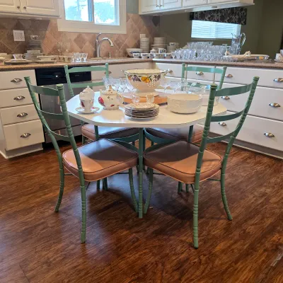 Hexagonal kitchen table and green metal chairs with upholstered seats, displayed with china and glassware.
