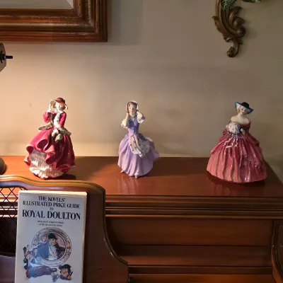 Royal Doulton porcelain figurines displayed atop the piano, featuring seated and standing ladies in colorful gowns.