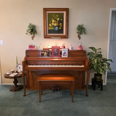 Kranich & Bach upright piano with matching bench, surrounded by porcelain figurines and framed floral artwork