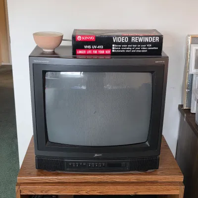 Vintage CRT television with a boxed VHS video cassette rewinder.