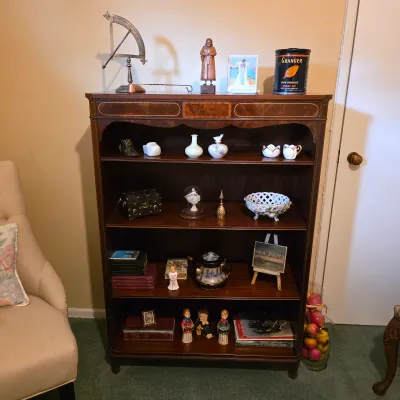 Traditional wood display bookcase with decorative trim, porcelain miniatures, books and small collectibles.