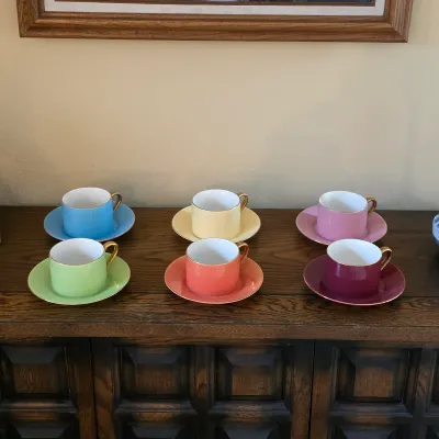 Six colorful cups and matching saucers in blue, yellow, pink, green, coral and burgundy.