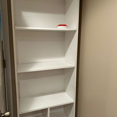 Sale Photo Thumbnail #69: Tall white laminate bookcase featuring adjustable upper shelves and divided lower cubby compartments.