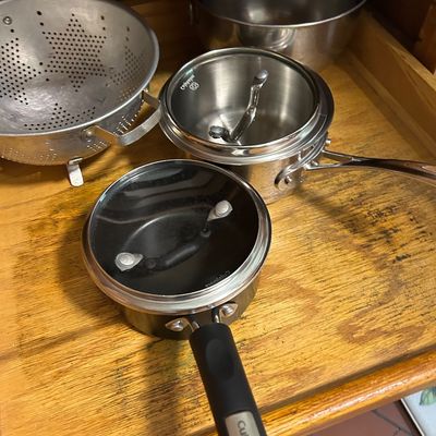 Sale Photo Thumbnail #18: Assorted kitchen cookware including a Cuisinart non-stick saucepan with lid, a stainless steel Calphalon saucepan with lid, a metal colander, and a stainless steel mixing bowl.