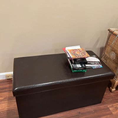 Sale Photo Thumbnail #66: Dark brown faux leather storage ottoman bench, shown with a small stack of media items on top.