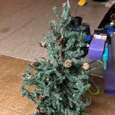 Sale Photo Thumbnail #76: Small pre-lit artificial Christmas tree decorated with pinecones, standing on a tiled floor.