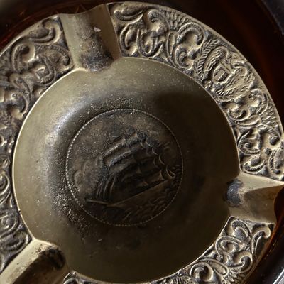 Sale Photo Thumbnail #56: Vintage brass ashtray featuring an embossed sailing ship in the center and ornate scrollwork along the rim.