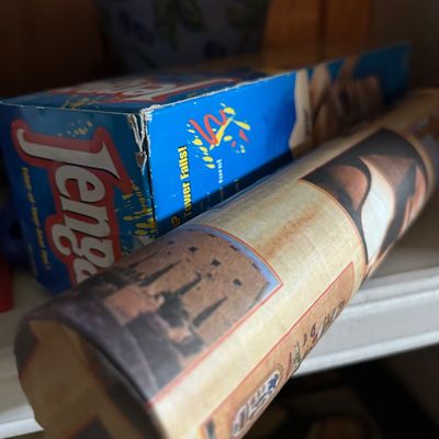 Sale Photo Thumbnail #96: Vintage Jenga board game in its original blue box, shown alongside a rolled poster or map on a shelf.