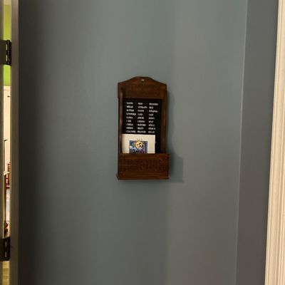 Sale Photo Thumbnail #100: Vintage wooden wall-mounted grocery list reminder board with a small storage pocket, mounted on a blue wall.