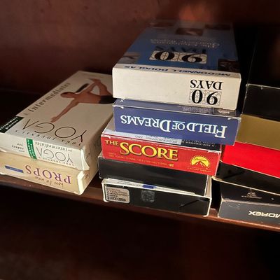 Sale Photo Thumbnail #95: Assorted VHS tapes on a wooden shelf, including "Field of Dreams," "The Score," and yoga instructional videos.