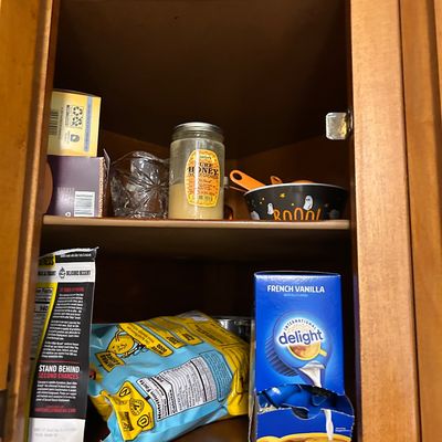 Sale Photo Thumbnail #16: Assorted pantry items and kitchenware inside a wooden cabinet, including a jar of Gunter's Pure Honey, a Halloween-themed bowl, and packaged food items.