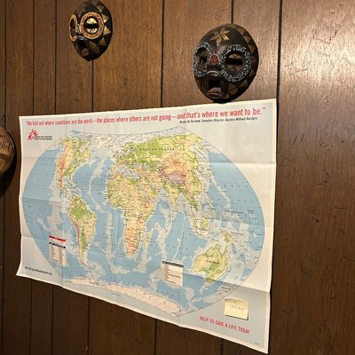 Sale Photo Thumbnail #77: Doctors Without Borders promotional world map poster displayed on a wood-paneled wall below two decorative African-style beaded masks.