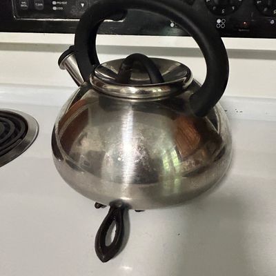 Sale Photo Thumbnail #28: Stainless steel stovetop tea kettle with a black heat-resistant handle and lid knob, showing light surface wear.