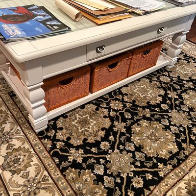 Sale Photo Thumbnail #70: White painted wooden coffee table featuring a glass top insert, two drawers, turned legs, and a lower shelf holding three woven wicker storage baskets, positioned over a traditional patterned area rug.