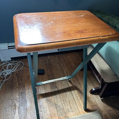 Sale Photo Thumbnail #102: Vintage folding TV tray table featuring a wooden top with rounded edges and a green-painted metal frame, showing moderate wear and surface scratches.
