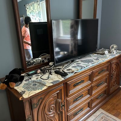 Sale Photo Thumbnail #107: Vintage Mediterranean-style wooden triple dresser featuring ornate carved cabinet doors, brass hardware, and dual matching mirrors.