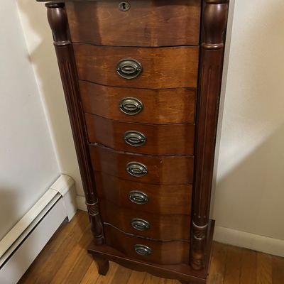 Sale Photo Thumbnail #110: Traditional dark wood standing jewelry armoire featuring a serpentine front with seven drawers, brass hardware, and fluted side columns.