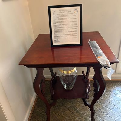 Sale Photo Thumbnail #132: Traditional mahogany-finish side table featuring cabriole legs, a lower shelf with a glass vase, and a framed document on top.