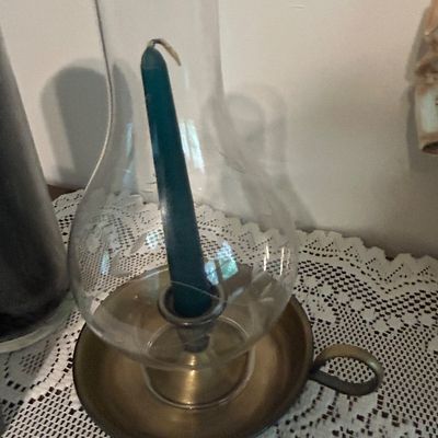 Sale Photo Thumbnail #27: Vintage brass chamberstick candle holder featuring a finger loop handle, a clear glass hurricane chimney with etched floral details, and a teal taper candle.