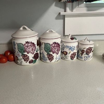 Sale Photo Thumbnail #31: Four-piece ceramic kitchen canister set featuring a floral motif with hydrangeas and wildflowers, in graduated sizes with matching lids.