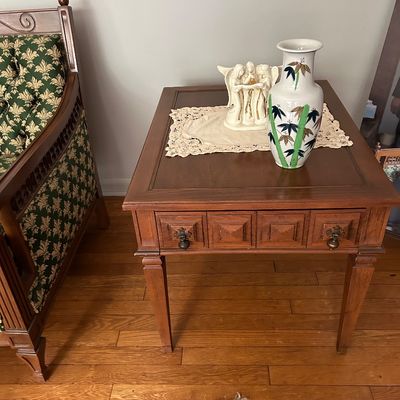 Sale Photo Thumbnail #140: Vintage wooden end table with a single drawer featuring geometric paneling and brass pulls, styled with a ceramic vase and angel figurine.