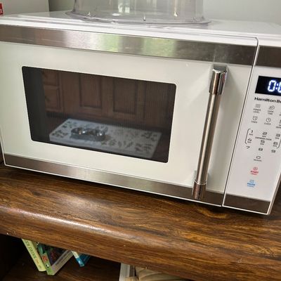 Sale Photo Thumbnail #98: Hamilton Beach countertop microwave in white and stainless steel, topped with a clear plastic splatter guard.