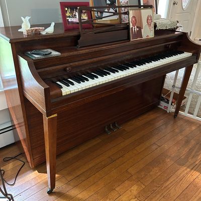 Sale Photo Thumbnail #142: Kimball spinet piano in a dark wood finish, featuring tapered legs on casters and a built-in music stand.