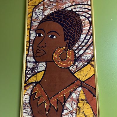 Sale Photo Thumbnail #84: African batik fabric art depicting a woman's portrait, framed in a simple gold-tone metal frame.