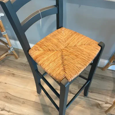 Sale Photo Thumbnail #88: Farmhouse-style counter stool featuring a dark gray painted wooden frame, ladder-back design, and a woven rush seat.