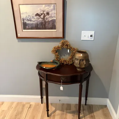 Sale Photo Thumbnail #87: Traditional dark wood demi-lune console table with a single drawer, styled with a multi-face bronze-tone vase, a star-shaped twig wreath, and a duck-shaped dish, beneath a framed eagle landscape print.