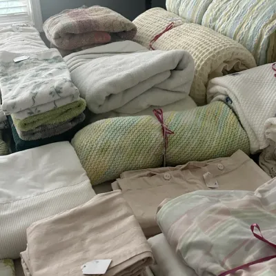 Sale Photo Thumbnail #128: Assortment of vintage and modern bed linens, blankets, and towels in pastel tones, some tied with ribbons and tagged for sale.