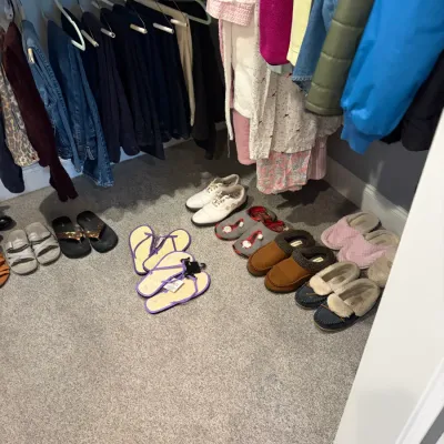Sale Photo Thumbnail #47: Assortment of women's footwear, including slippers, sandals, and sneakers, displayed on a closet floor beneath hanging clothing.