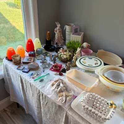 Sale Photo Thumbnail #102: Assorted vintage kitchenware and seasonal decor, featuring Pyrex mixing bowls, a ceramic woven basket with lemon accents, Easter bunny figurines, and colorful egg-shaped candles.