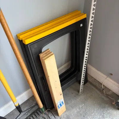 Sale Photo Thumbnail #179: Pair of black and yellow plastic folding sawhorses leaning against a wall, shown alongside a stack of wood boards and garden hand tools.